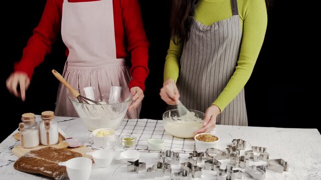 Two people preparing cookie dough together, whisking ingredients in glass bowls surrounded by baking tools and cutters, capturing a warm homemade baking atmosphere and collaborative kitchen