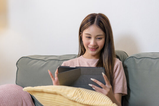Teen woman uses tablet happy person relaxing comfortably reading digital content enjoying modern technology at home soft sofa cozy blanket visible.