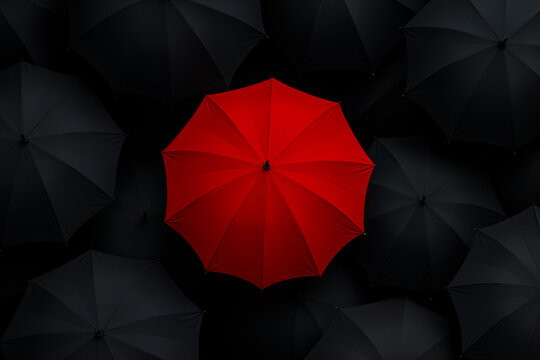 Elevated view captures a bold red umbrella amidst a sea of black ones, symbolizing uniqueness in uniformity, standing out, and individuality.