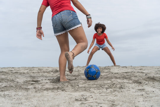 Girls playing soccer barefoot on beach sand