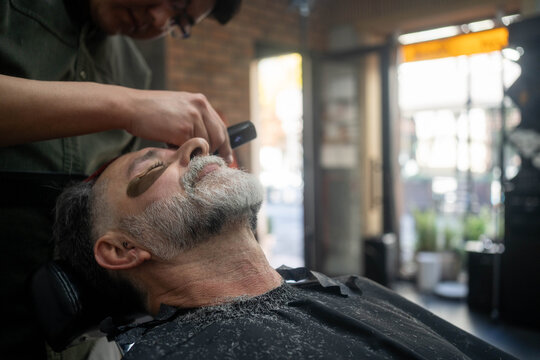 Barber using wax for precise facial hair removal on client, professional grooming in barber shop