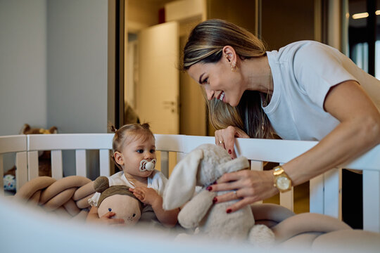 Mother interacting with her baby in a crib, sharing a happy moment with stuffed toys during playtime at home