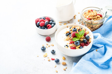 Yogurt with fresh berries and granola on white table.