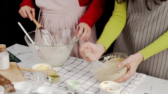 Two people mixing cookie dough together in glass bowls with flour, butter, matcha powder, and tools around them, capturing a warm homemade baking moment and collaborative kitchen