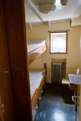 Explore the vintage quarters of a ship with bunk beds and a round porthole window providing natural light