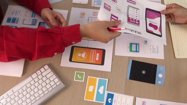 Excellent startup company employee presenting user interface prototype for mobile application to smart co-worker in office workspace. UX UI designer explain function of icon design on paper. Synergic