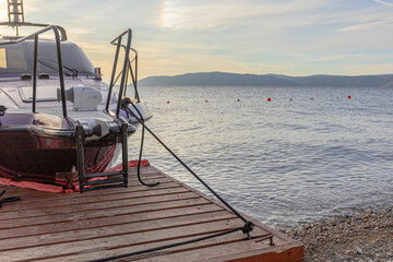 A sleek motorboat tied to a wooden dock along a tranquil lake at dusk in the background of distant mountains and a soft sky. Relaxation, travel, and outdoor leisure.