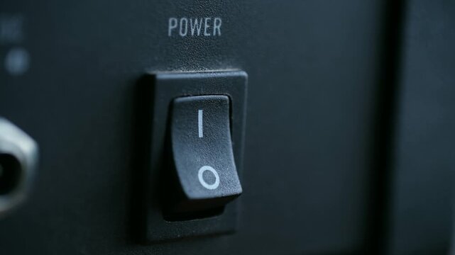 closeup switch operation, studio scene capturing technician testing power control with tactile switch, fingertip presses matte black rocker switch amid lowlight and textured plastic environment