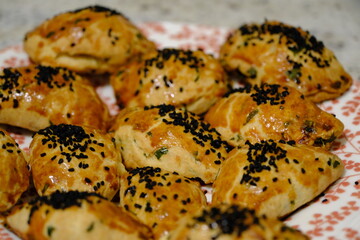 Macro and close-up shot of delicious homemade black cumin pastries. Turkish pastries. Breakfast pastries with cheese and parsley, made by a housewife, on a red plate. Traditional delicacies.