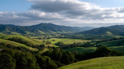 Obraz premium A breathtaking panoramic view of a lush verdant valley nestled between rolling green hills and distant mountains under a dramatic cloud filled sky