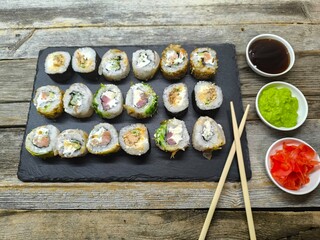 Close-up of various sushi lying on granite board next to wooden chopsticks and various sauces
