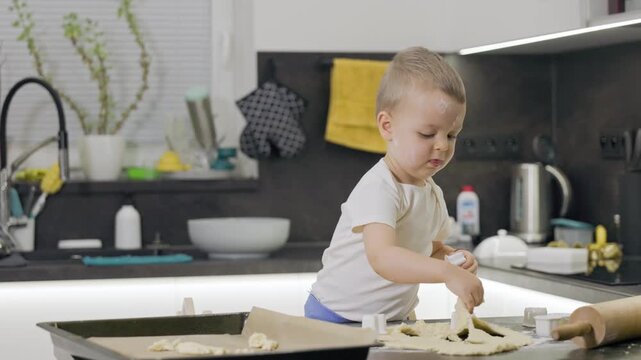 Adorable little toddler boy making cookies in the kitchen