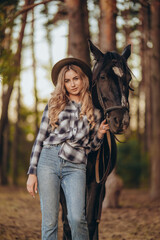 Fototapeta premium A young beautiful woman walks with her horse in the forest in early autumn. Walking with a horse in the forest.