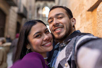 Latino couple happily traveling, smiling for a selfie on a city street during vacation