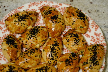 Macro and close-up shot of delicious homemade black cumin pastries. Turkish pastries. Breakfast pastries with cheese and parsley, made by a housewife, on a red plate. Traditional delicacies.