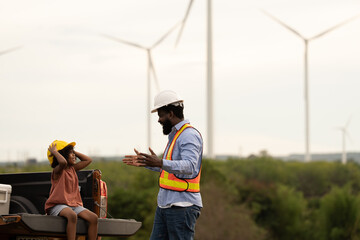 Engineer father and daughter wearing safety vests and hard hats sharing a joyful moment at wind turbine site, symbolizing family bonding, renewable energy learning, and STEM career inspiration. © Montri