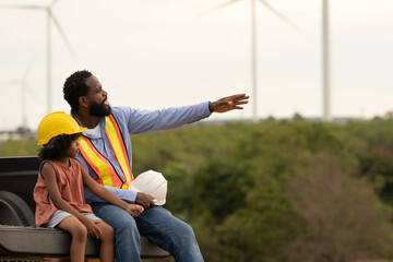 African American engineer father pointing at wind turbines while sitting with daughter, symbolizing guidance, renewable energy education, family connection, and inspiring future in clean technology.