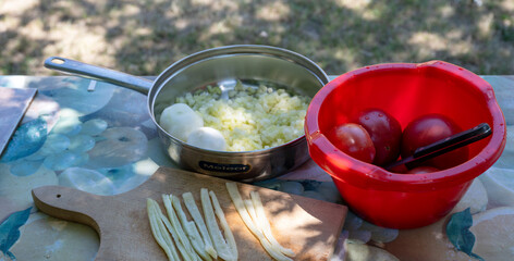 Outdoor food preparation with fresh vegetables. Chopped onions, sliced peppers, and tomatoes on a table with a knife and cutting board. Concept of healthy cooking and rustic kitchen lifestyle.