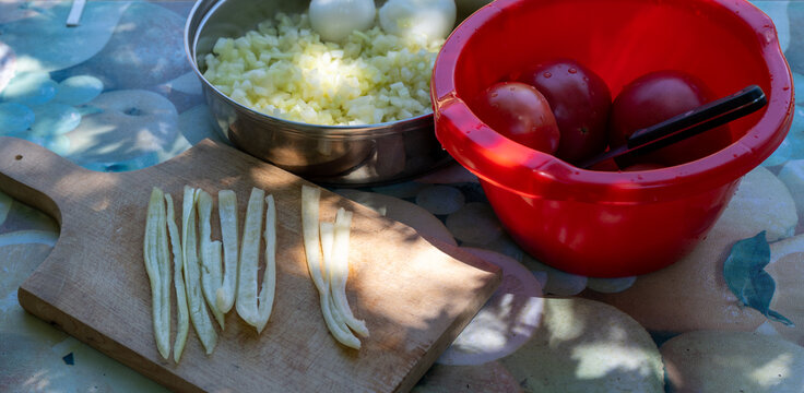 Outdoor food preparation with fresh vegetables. Chopped onions, sliced peppers, and tomatoes on a table with a knife and cutting board. Concept of healthy cooking and rustic kitchen lifestyle. - Powered by Adobe