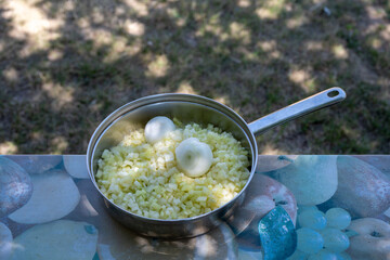 Rustic outdoor cooking scene with chopped bell pepper and two whole heads of garlic in a frying pan on a colorful table. Fresh vegetables ready for cooking or preparing a salad. Concept of healthy, or