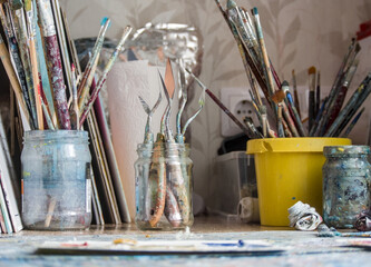 Artist's paint brushes - A messy artist's desk with numerous paintbrushes of all sizes in glass jars and buckets