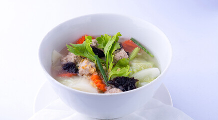 Clear soup with Chinese cabbage, seaweed, minced pork cubes, carrots, spring onions, and clear broth, placed in a white bowl, white background.