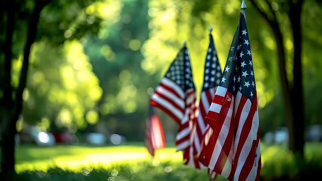 A closeup of American flags in a park setting, with a bokeh effect from the sunlight filtering through the trees. The flags are prominently displayed against a backdrop of lush green foliage.