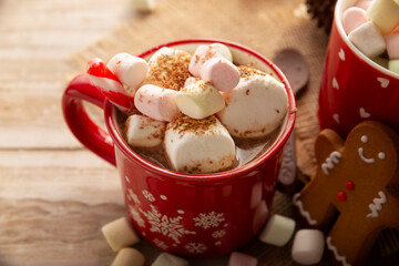Hot chocolate with marshmallows, a traditional hot drink made for Christmas time and holidays. Served in a red mug and accompanied by gingerbread men cookies.