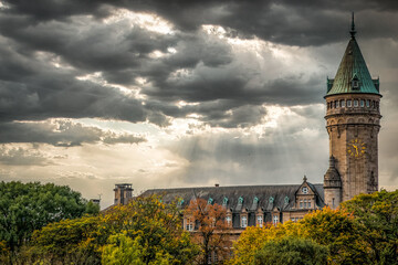 Historic Spuerkeess building in Luxembourg City under dramatic storm clouds, with sunlight breaking...