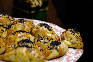 Macro and close-up shot of delicious homemade black cumin pastries. Turkish pastries. Breakfast pastries with cheese and parsley, made by a housewife, on a red plate. Traditional delicacies.