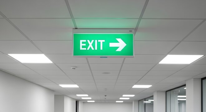 Illuminated green exit sign with arrow for emergency guidance in modern office hallway ceiling design