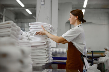 A woman worker is stacking towels neatly on a table in a laundromat
