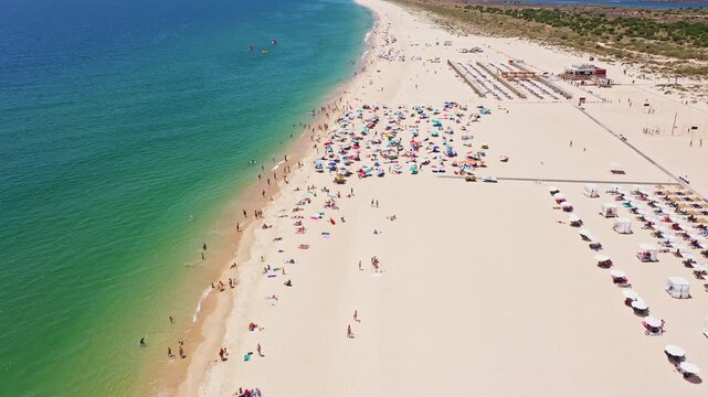 Aerial view drone shot of Tavira Portugal Algarve Aerial view crowded sandy beach umbrellas turquoise sea, colorful umbrellas dot shoreline, sunbathers and families relax under parasols,