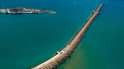 An aerial view of a pier at the exit of a port. The sea is crystal blue.