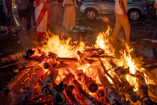 Close up macro shot of wooden logs covered in ash burning with a bright orange warm flame showing outdoor camping, winter nights and the hindu festival of Holi