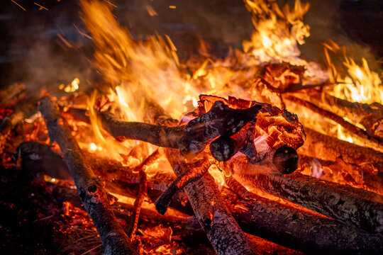 Close up macro shot of wooden logs covered in ash burning with a bright orange warm flame showing outdoor camping, winter nights and the hindu festival of Holi