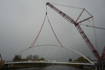 Massive Red Lattice Crane Carefully Lifts A New White Arched Section Of The Waterside Bridge Over The Trent Basin In Nottingham On A Grey, Overcast Day.