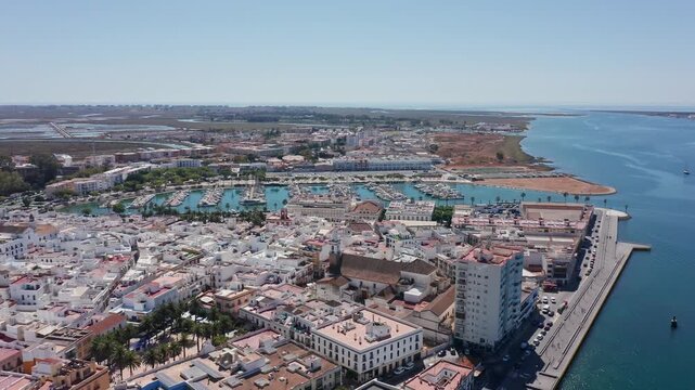 Aerial view drone shot of Ayamonte Aerial view harbor skyline and azure bay with tall waterfront building, marina docks, estuary mouth and wide clear horizon for dramatic composition.