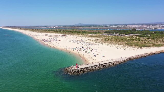 sunny tavira sand beach with umbrellas, colorful sunshades and packed shoreline along protective jetty tourists lounging, families playing near turquoise ria formosa waters, dunes
