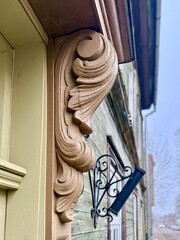 Decorative wooden corbel on a historic building facade, featuring ornate carved details and a wrought-iron wall bracket on a street in an old town.  © Kristine