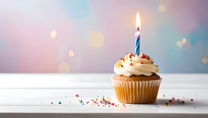Frosted cupcake with lit candle and colorful sprinkles sits atop a clean white surface with a pastel bokeh background