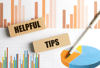 Wooden blocks with the words helpful tips on financial charts background with pen, representing advice