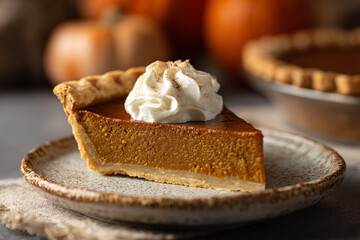 Delicious slice of pumpkin pie with whipped cream on a rustic plate.
