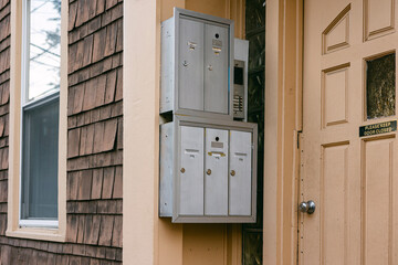 Multiple mailboxes attached to a residential building entrance with a doorbell panel nearby