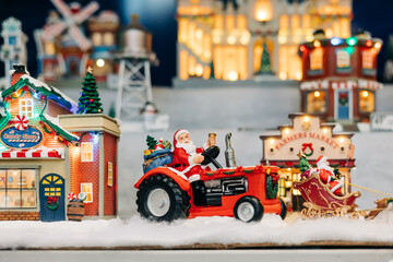 Santa drives a tractor through a festive miniature village scene during the holiday season