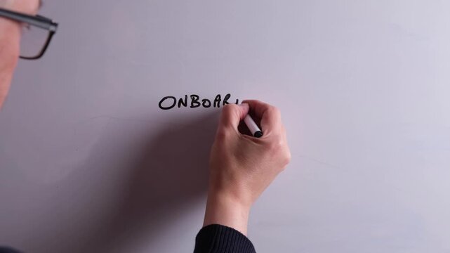 An HR business professional is writing Onboarding Process on a whiteboard in black marker pen, ideal for HR, recruitment, and business workplace presentations.