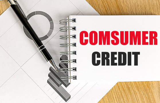 Consumer credit text with spelling mistake written on notebook with financial charts and black pen on wooden desk