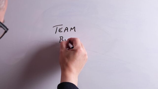 An HR business professional is writing Team Building on a whiteboard in black marker pen, ideal for HR, recruitment, and business workplace presentations.
