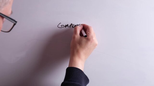 An HR business professional is writing Compensation and Benefits on a whiteboard in black marker pen, ideal for HR, recruitment, and business workplace presentations.