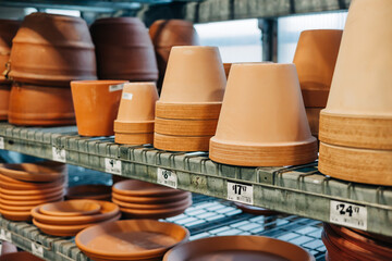 Clay pots and dishes arranged neatly on shelves in a garden supply store during a sunny day